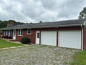 A two-story house with a garage, a front door, and a small front yard with a gravel path.