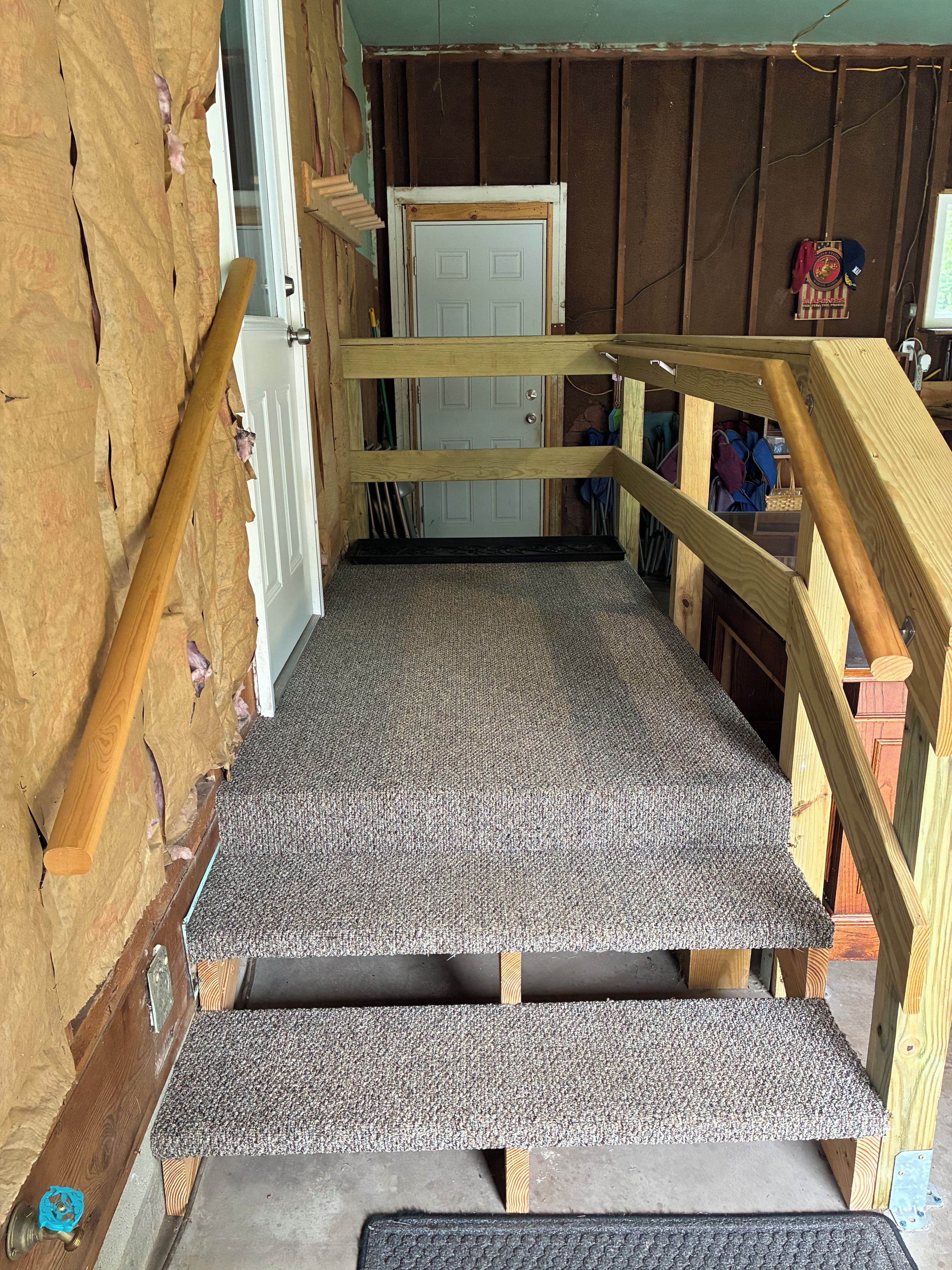 A wooden staircase with a carpeted landing leading to a door.