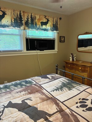 A bedroom with a bed, a dresser, a window with blinds, and a wall with a deer and forest mural.