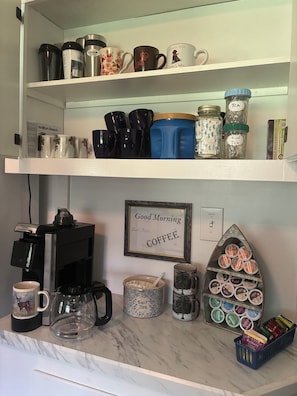 Un taulell de cuina amb una cafetera, tasses, un pot de sal i un cartell emmarcat que diu 'Good Morning COFFEE'.