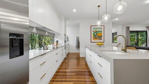 A modern kitchen with a built-in dishwasher, a wooden floor, and pendant lighting. - Serenity Escape - Private, Pet-Friendly Home on the Broadwater (Bilambil Heights)