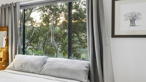 Una camera da letto con una grande finestra, un letto con cuscini a righe e un quadro appeso al muro.
