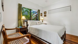 A hotel room with a bed, two bedside lamps, a chair with a woven seat, a window with curtains, and a wall-mounted picture frame. - Serenity Escape - Private, Pet-Friendly Home on the Broadwater (Bilambil Heights)