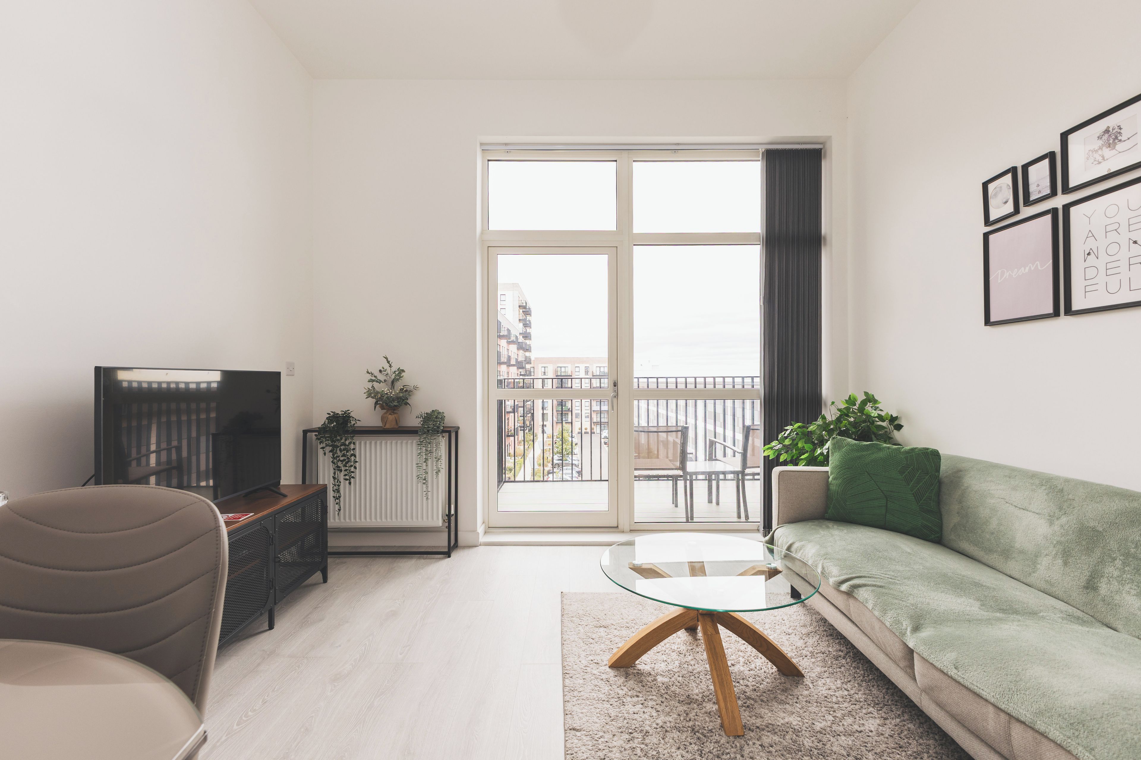 Ein modernes Wohnzimmer mit einer Couch, einem Glastisch, einem Fernseher und einem Heizkörper mit Pflanzen.