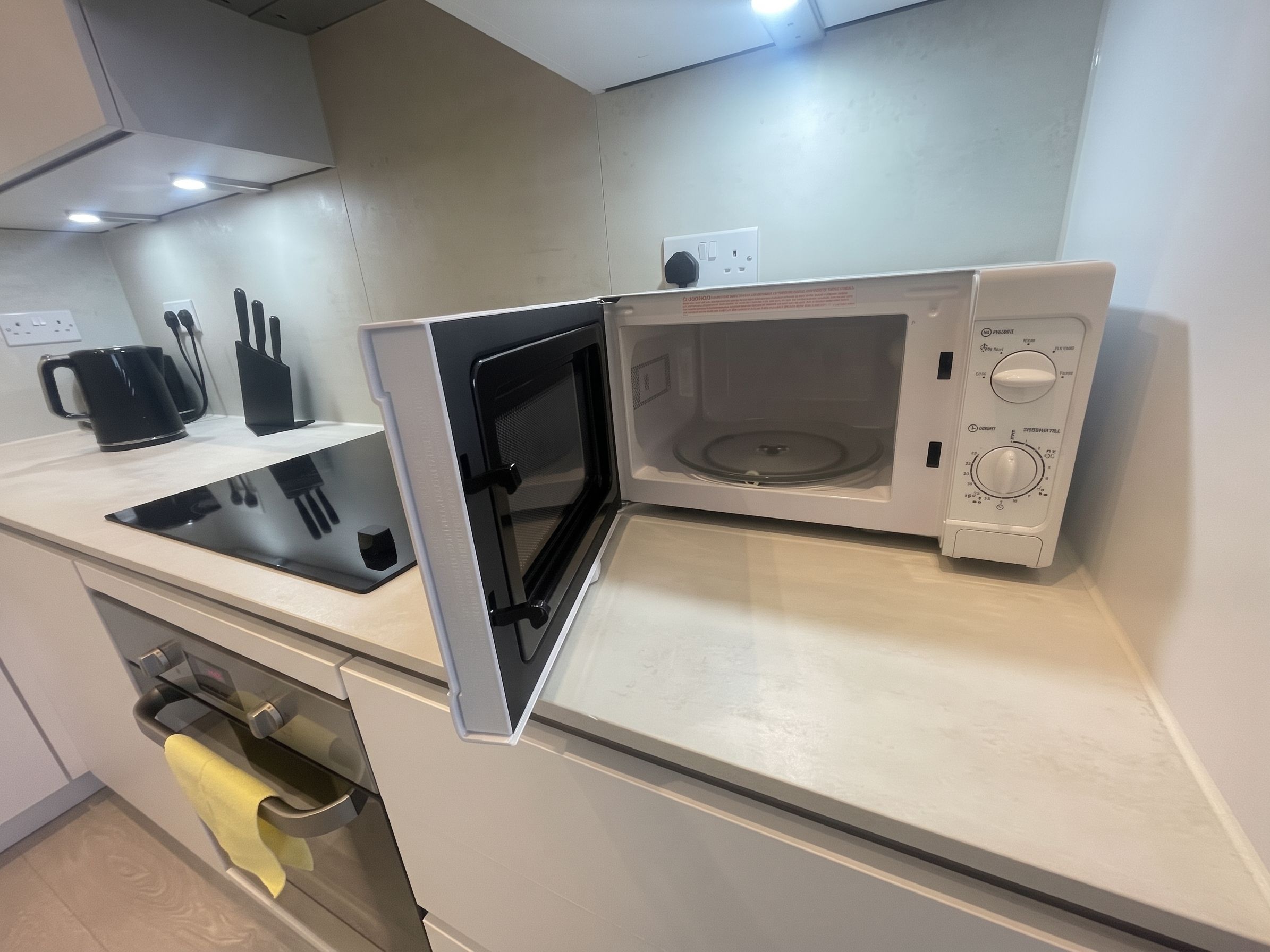 A kitchen with a microwave, a kettle, and a knife block.