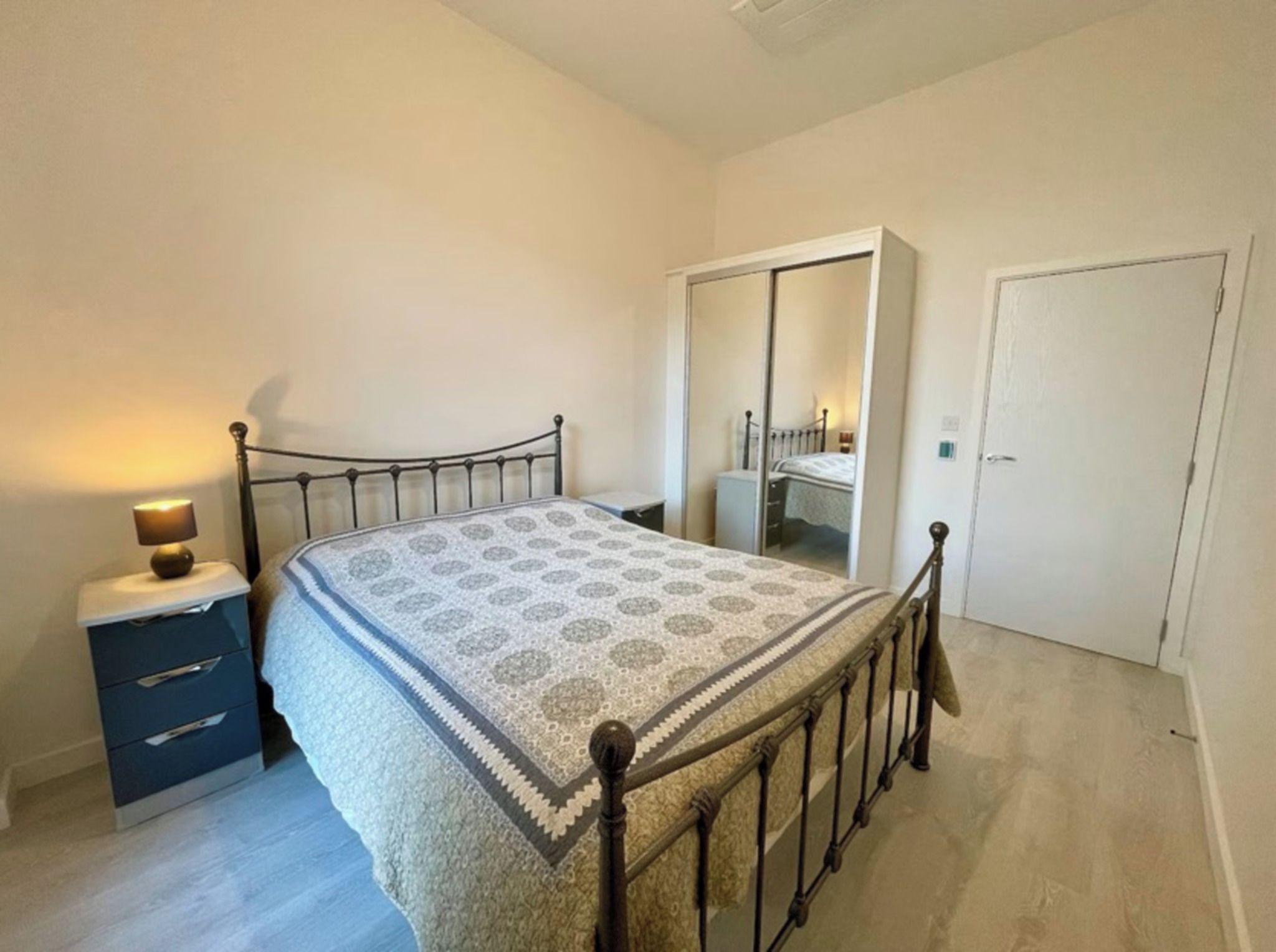 Un dormitorio con una cama, una mesita de noche, un armario y una puerta.