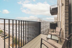 Ein Balkon mit Blick auf einen Parkplatz und Gebäude, ausgestattet mit einem Metallgeländer und einem Tisch mit Stühlen.