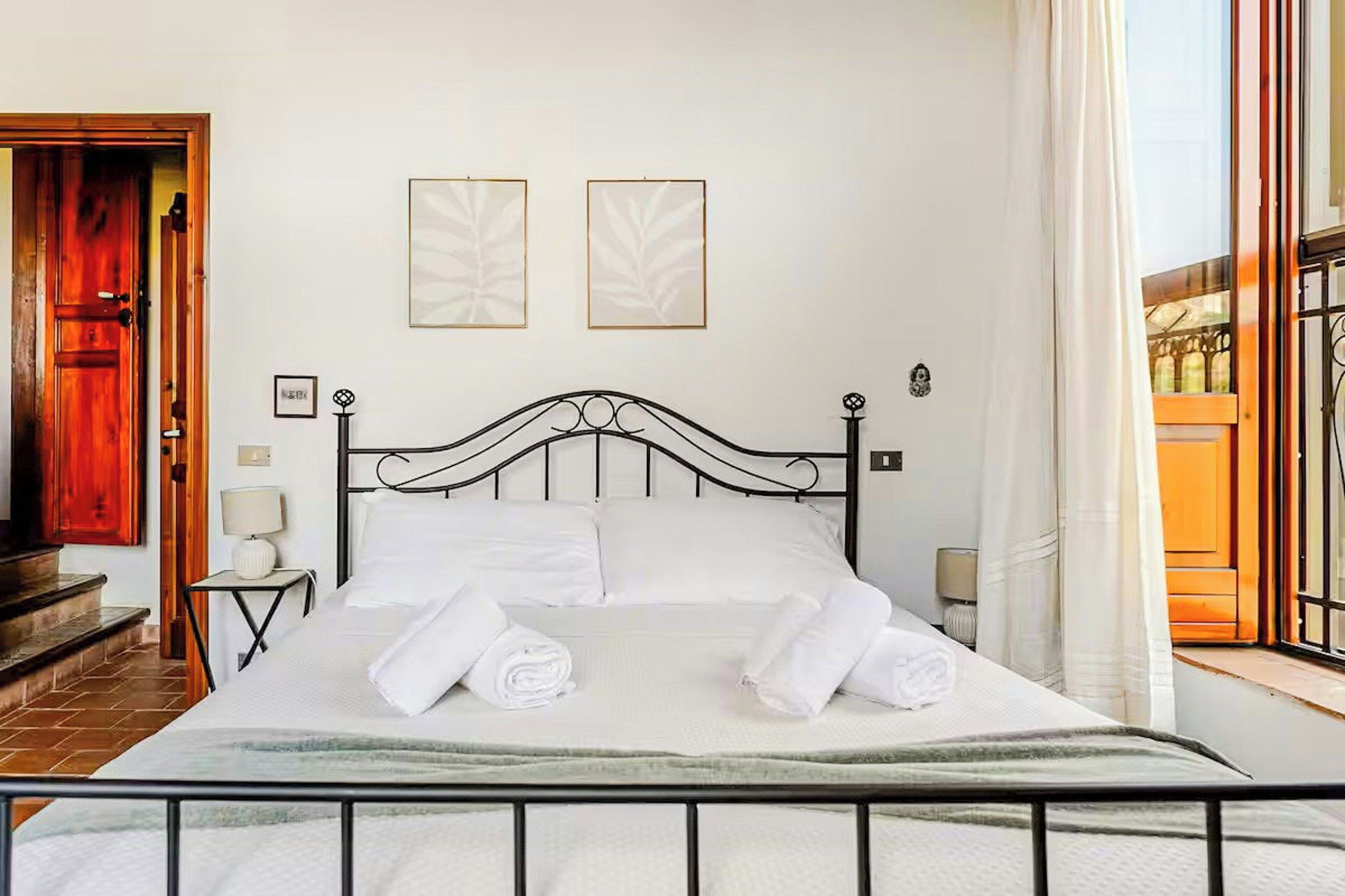 A neatly made bed with white linens and towels, a black metal headboard, and two framed artworks on the wall.