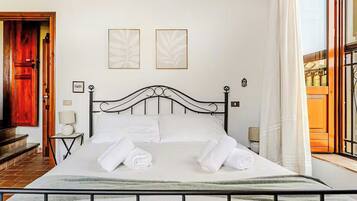 A neatly made bed with white linens and towels, a black metal headboard, and two framed artworks on the wall.