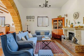 A living room with a sofa, armchair, coffee table, and a fireplace. There is a window with curtains, a chandelier, and a cabinet with dishes. - Family home in the UNESCO Valley of the Temples (Agrigento)