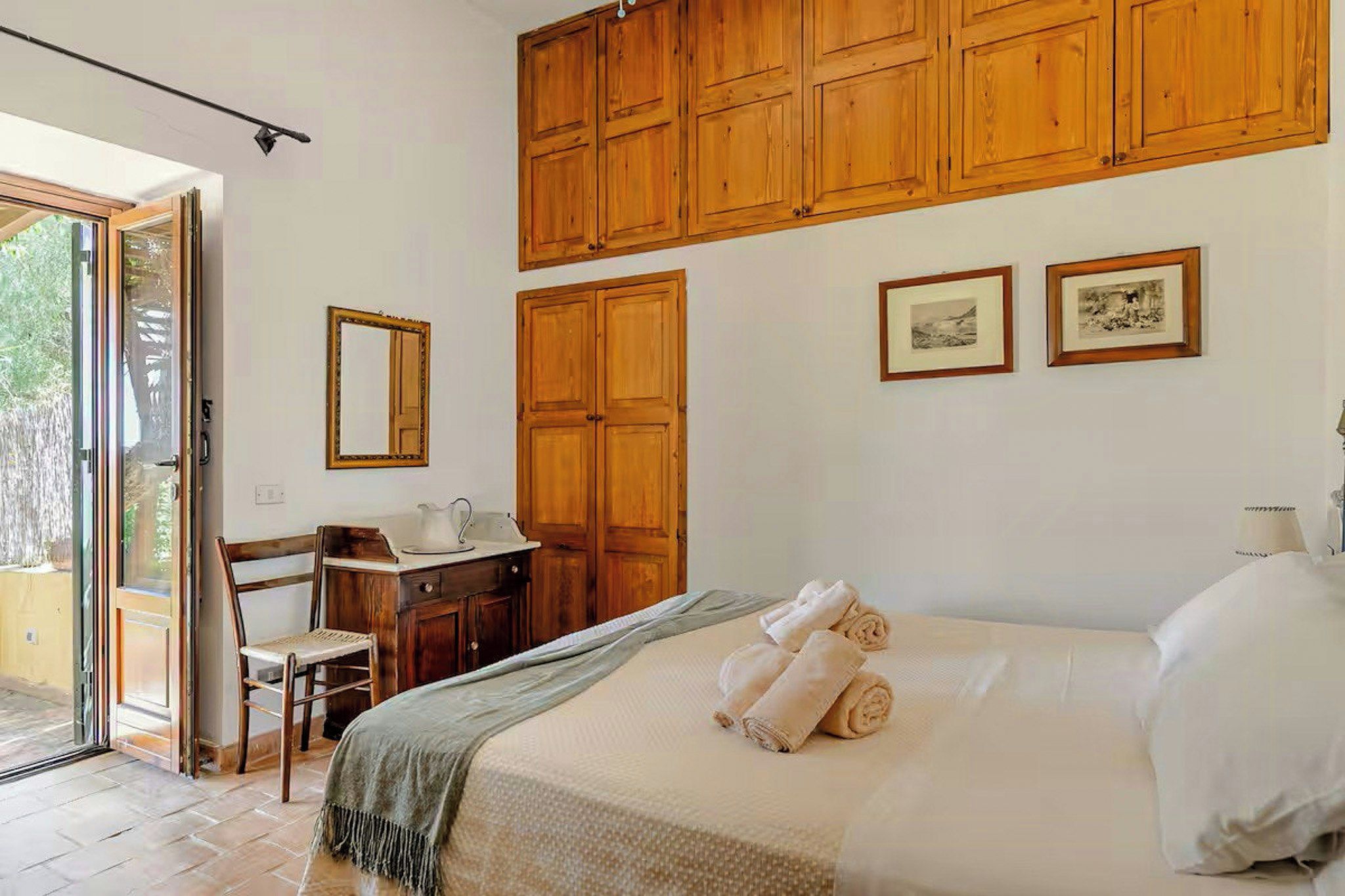 A bedroom with a bed, a desk, a chair, a mirror, and wooden cabinets.