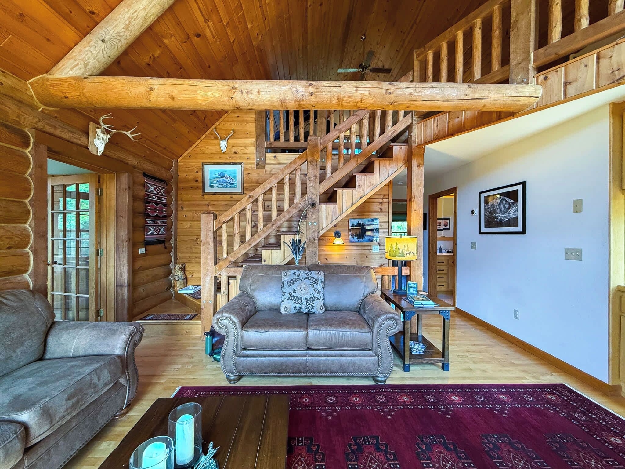 Ein Holzblockhaus-Interieur mit einer Holztreppe, einem Ledersofa und einem roten Teppich.
