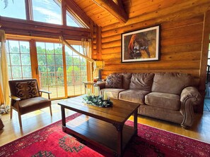 Ein gemütliches Blockhaus-Interieur mit Ledersofa, Holztisch und großem Fenster mit Blick ins Freie.