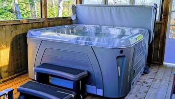 Un bain à remous avec des marches menant à celui-ci, installé sur une terrasse en bois et offrant une vue sur les arbres.