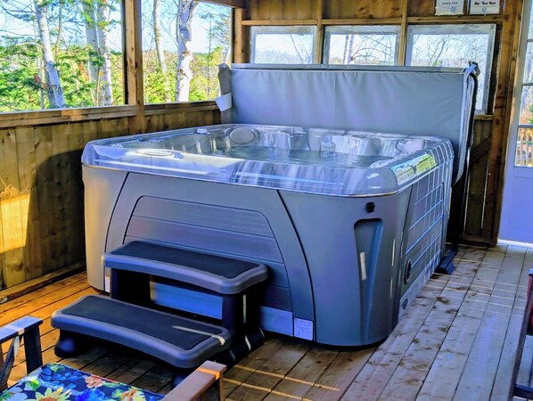 A hot tub with steps leading up to it, set on a wooden deck with a view of trees.
