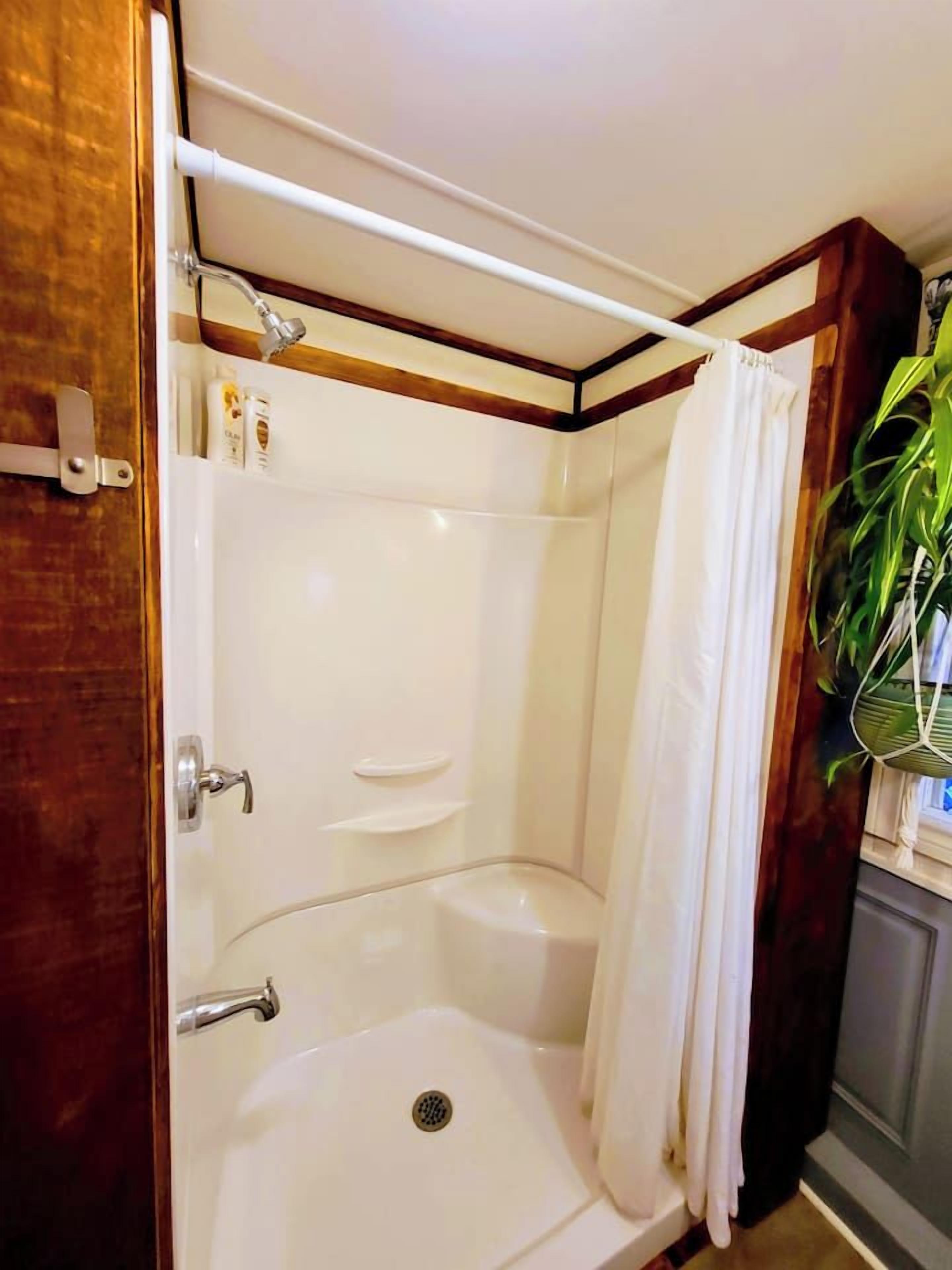 A corner shower with a white curtain, a handheld showerhead, and a small shelf.