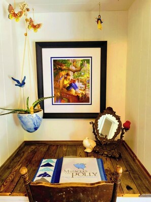 A framed picture on a wall, a hanging plant, a mirror, and a chair with a placemat.