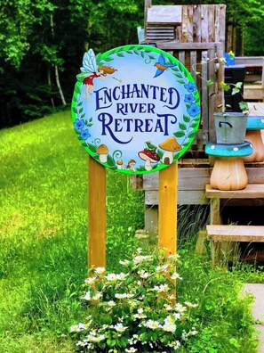 Ein rundes Schild mit dem Text 'Enchanted River Retreat', umgeben von naturbezogenen Illustrationen.