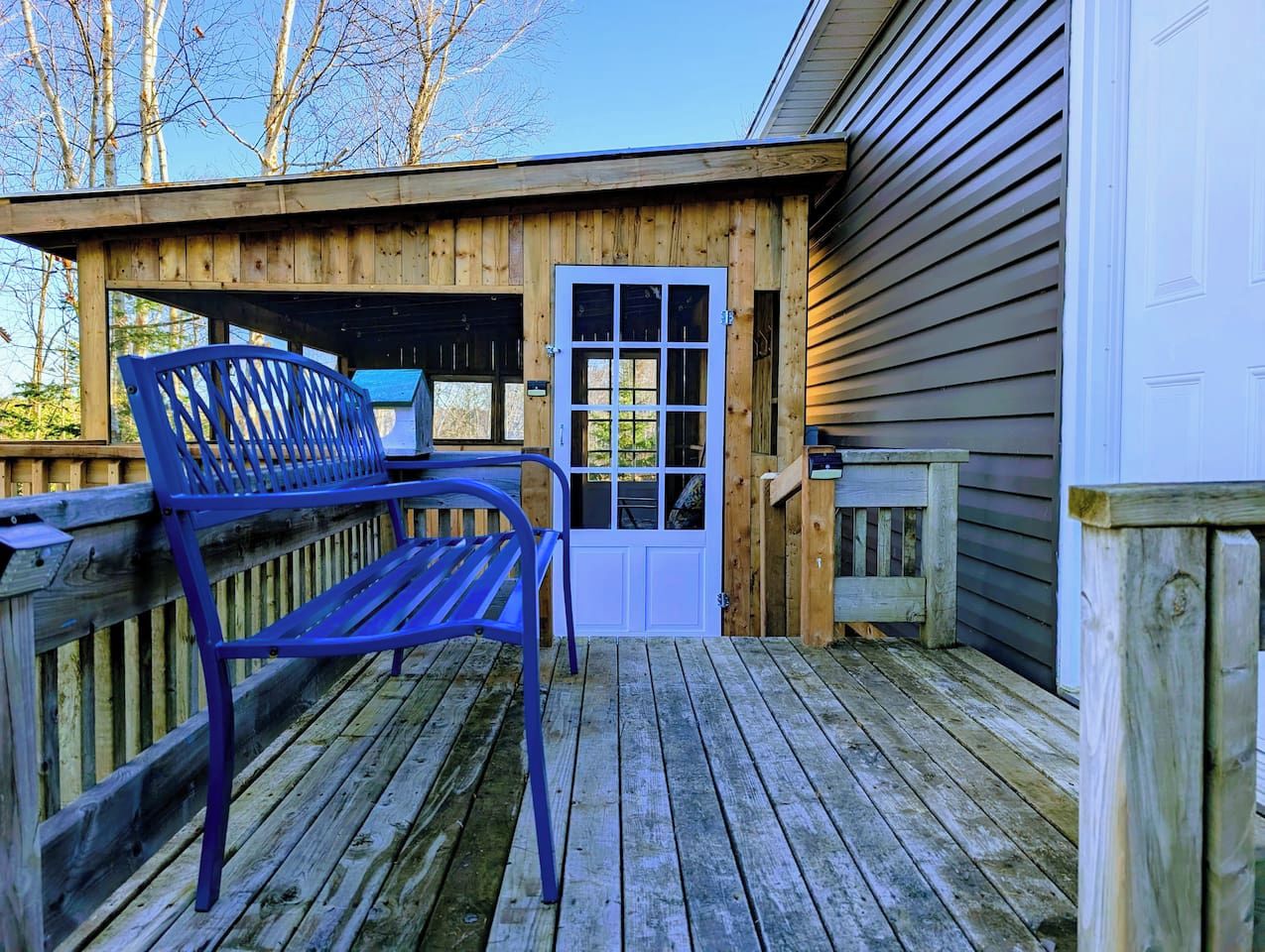 A wooden deck with a bench and a door leading to a building.
