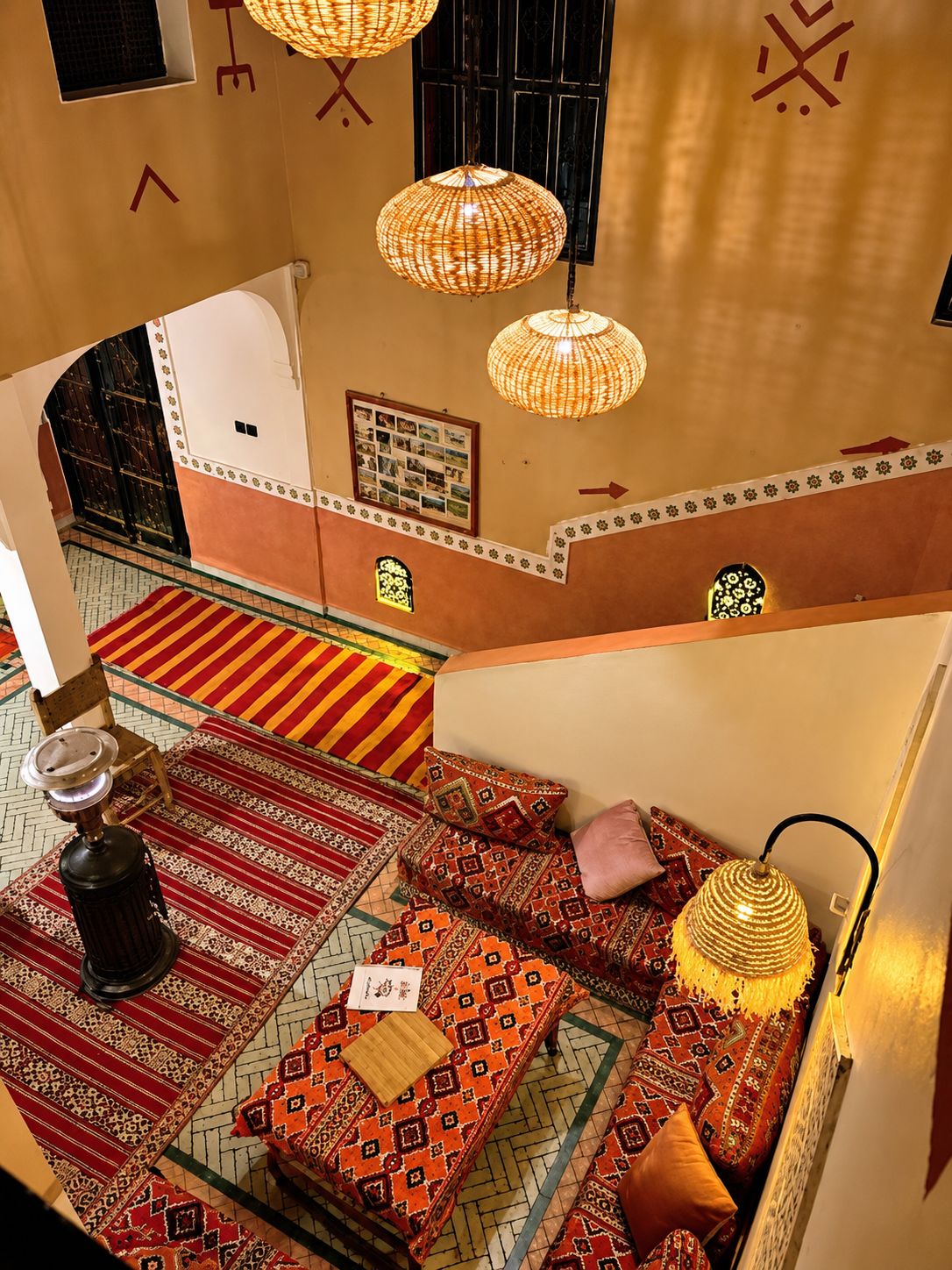 Une pièce au décor traditionnel, avec un sol à motifs, un lit avec des oreillers, une étagère fixée au mur et une lampe suspendue.