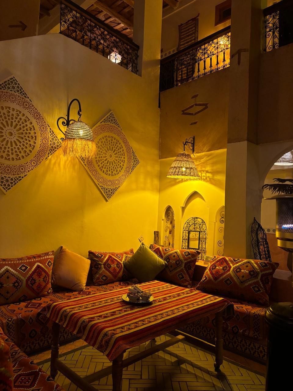 A traditional Moroccan interior with a sofa set, patterned cushions, and decorative wall lamps.