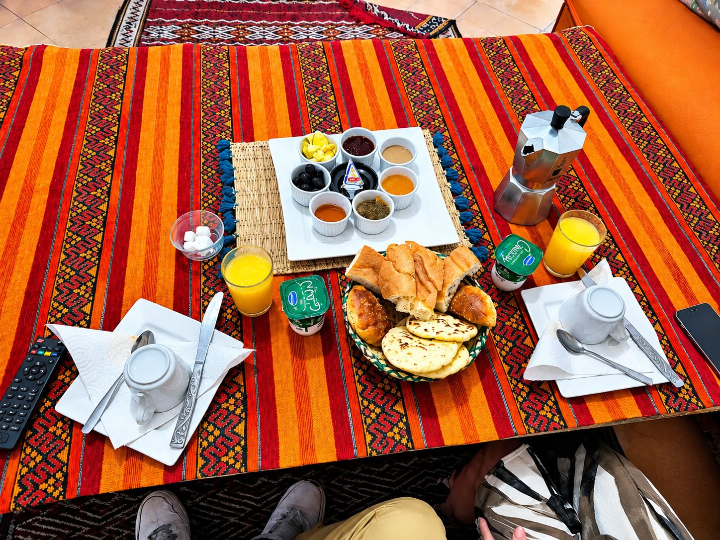 A breakfast setup with a variety of food items and drinks on a colorful tablecloth.