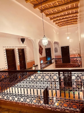An interior with a wooden ceiling, arched doorways, and a balcony with ornate metal railings. - auberge tissadrine (Ait Sedrate Jbel El Soufla)