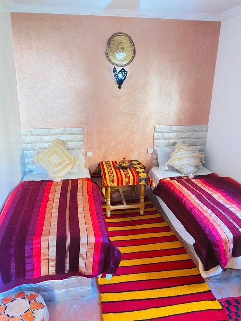 A room with two beds, a small table, and a decorative wall hanging.