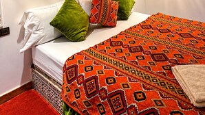 A bed with white linens and patterned pillows, a red carpet, and a decorative wall with a circular design. - auberge tissadrine (Drâa-Tafilalet)