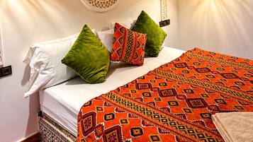 Un lit avec du linge de lit blanc et des coussins à motifs, une moquette rouge et un mur décoratif orné d’un motif circulaire.