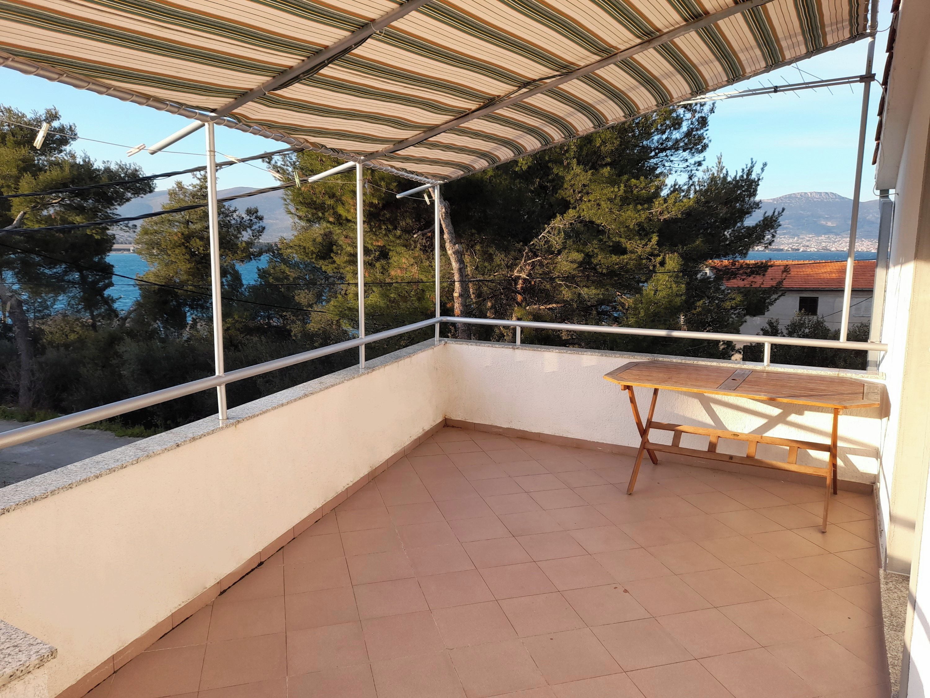 A balcony with a striped awning, a wooden table, and a view of trees and a distant mountain.