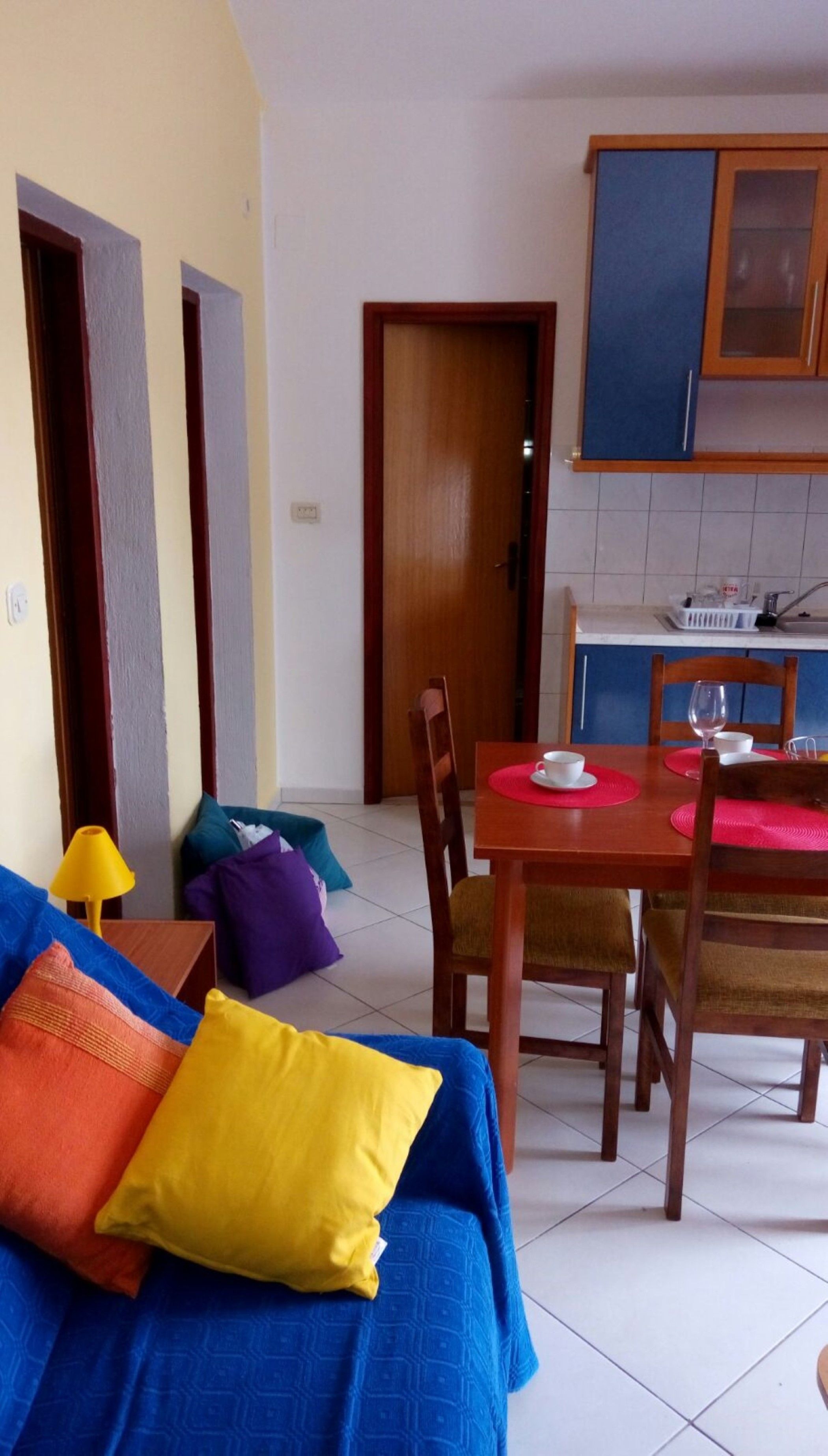 A living room with a blue sofa, a wooden dining table with chairs, and a kitchen area with cabinets and a sink.