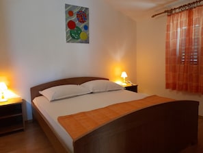 Een netjes opgemaakt bed met een houten hoofdbord, twee nachtkastjes met lampen, en een kleurrijk abstract schilderij aan de muur.