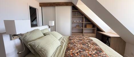A bedroom with a bed, a bedside table, a lamp, a window, and a built-in shelving unit.