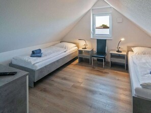 A small, triangular attic bedroom with two single beds, a desk, and a chair. - Holiday Home With 1 Bedroom (Esens)