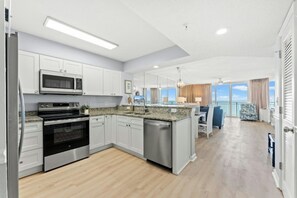 A modern kitchen with stainless steel appliances, a dining area with a view, and a balcony with a view. - Oceanfront 3BR- Windy Hill Dunes 705- Lazy River (North Myrtle Beach)