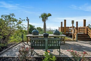 An outdoor patio with a wooden table, two barbecue grills, a bench, and a wooden deck with steps. - Oceanfront 3BR- Windy Hill Dunes 705- Lazy River (North Myrtle Beach)
