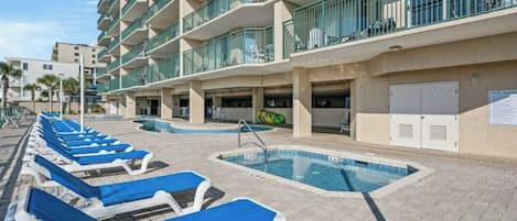 A hotel with multiple balconies, a swimming pool area with lounge chairs, and a parking garage.