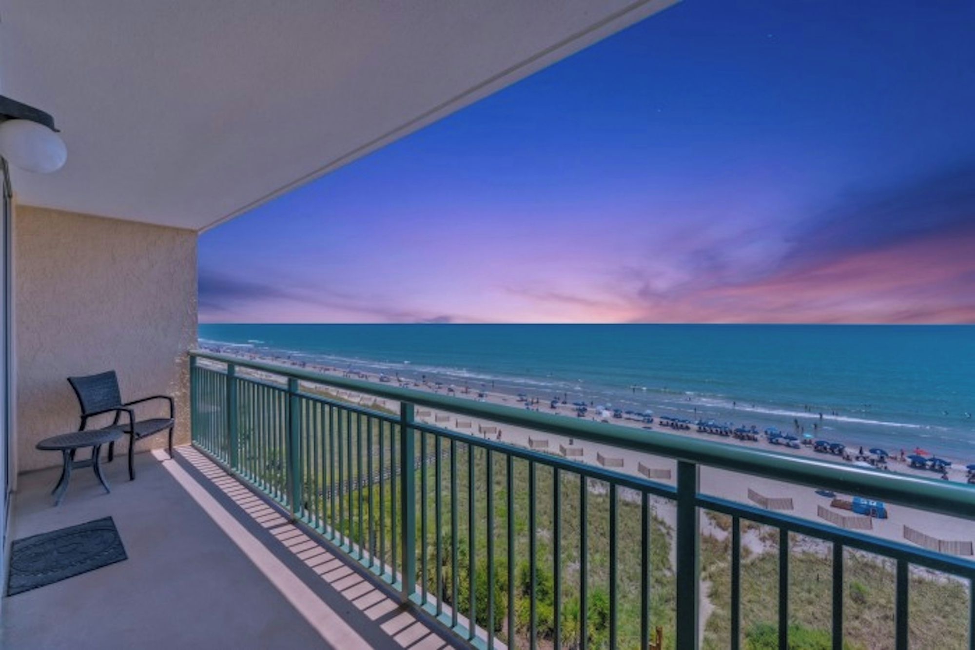 A balcony with a view of the beach and ocean during sunset.