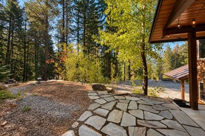 A stone pathway leading to a wooden structure with a sloped roof, surrounded by a forested area with tall trees and a clear sky. - New Listing|Forest|Sleeps 6 | BBQ Grill | Dogs OK (Leavenworth)