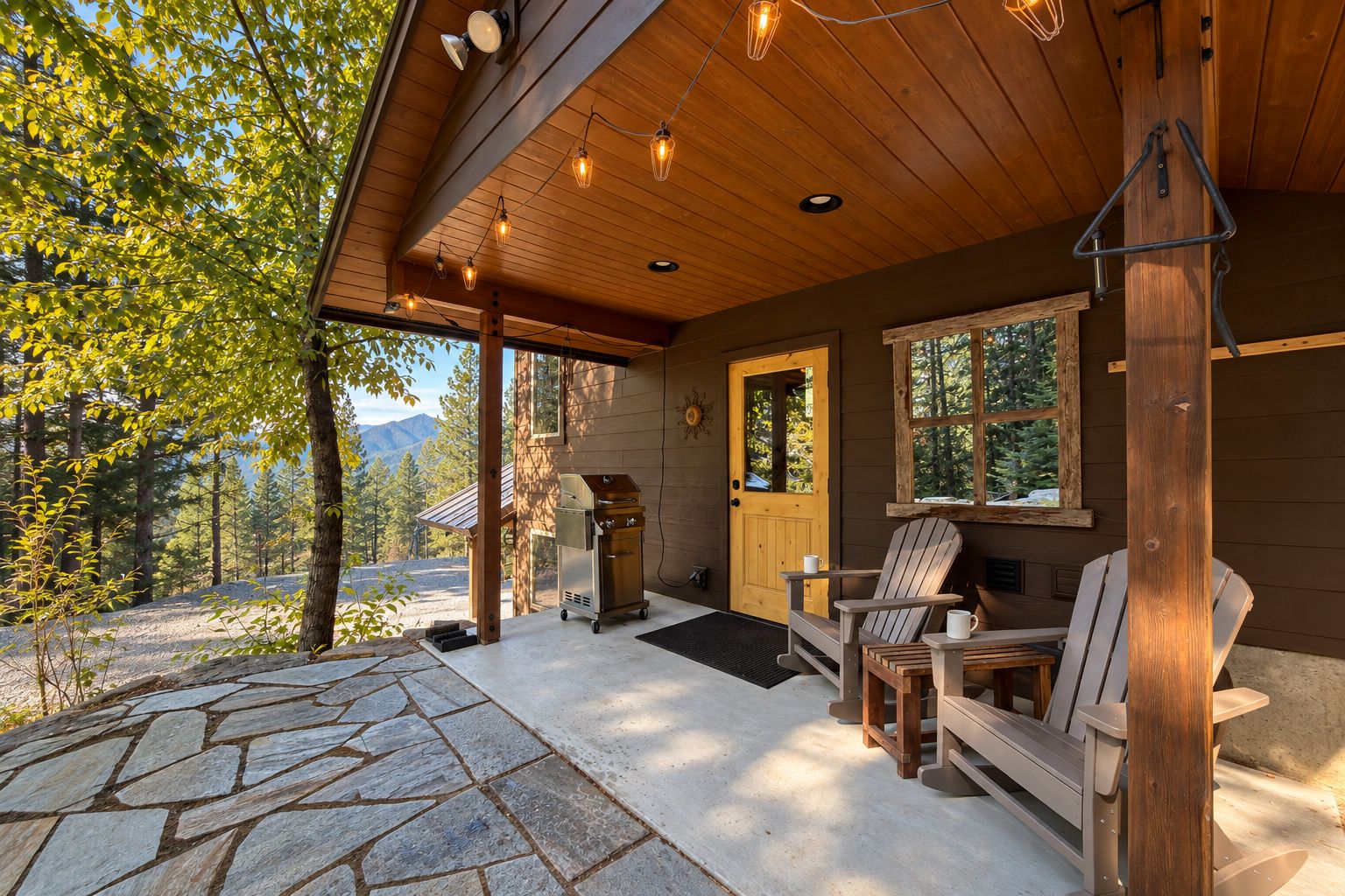 Eine Holzhütte mit einer terrasse aus Steinplatten, einem Grill und zwei Adirondack-Stühlen.