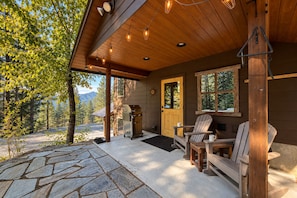 Eine Holzhütte mit einer terrasse aus Steinplatten, einem Grill und zwei Adirondack-Stühlen.