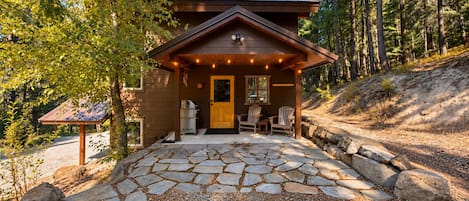 A cabin with a stone patio, wooden deck, and a covered seating area with chairs.