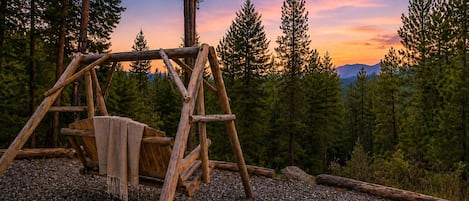A rustic wooden swing set in a forested area with a clear sky.
