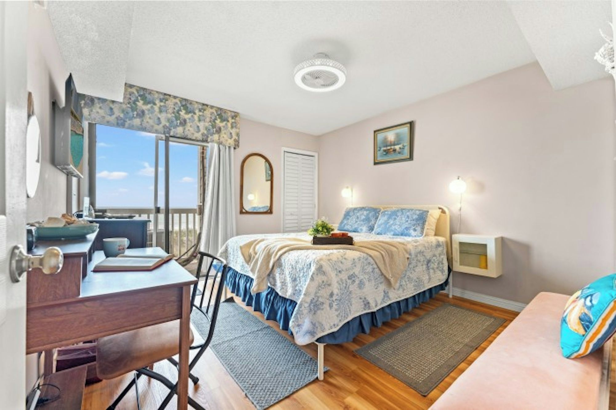A bedroom with a bed, bedside table, desk, chair, and a view of the outdoors.