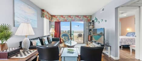 Una sala de estar con sofá, sillas, una mesa de centro, televisor y un balcón con vistas.
