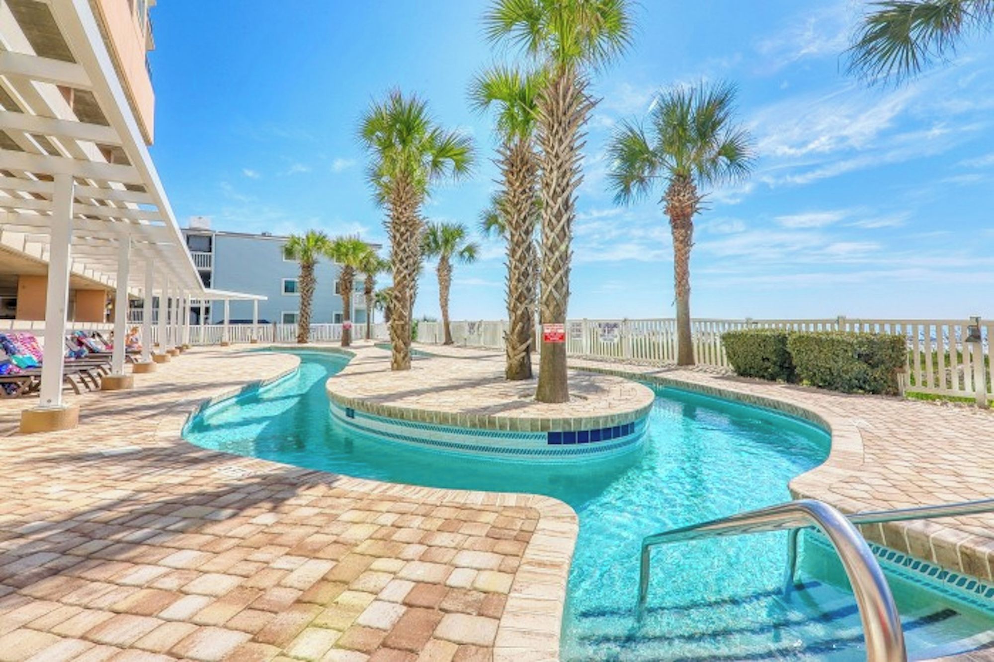 A pool area with palm trees, a white building, and a clear sky.