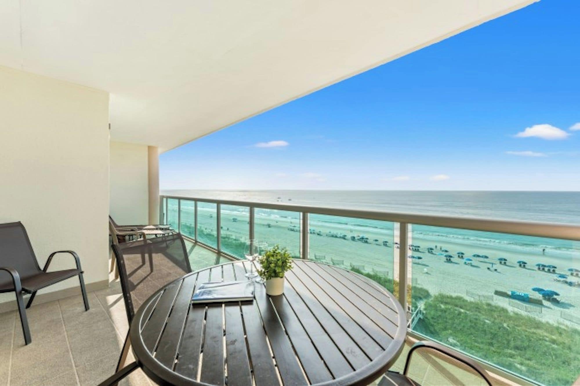 Een balkon met uitzicht op de oceaan, een ronde tafel met een plant en twee stoelen.