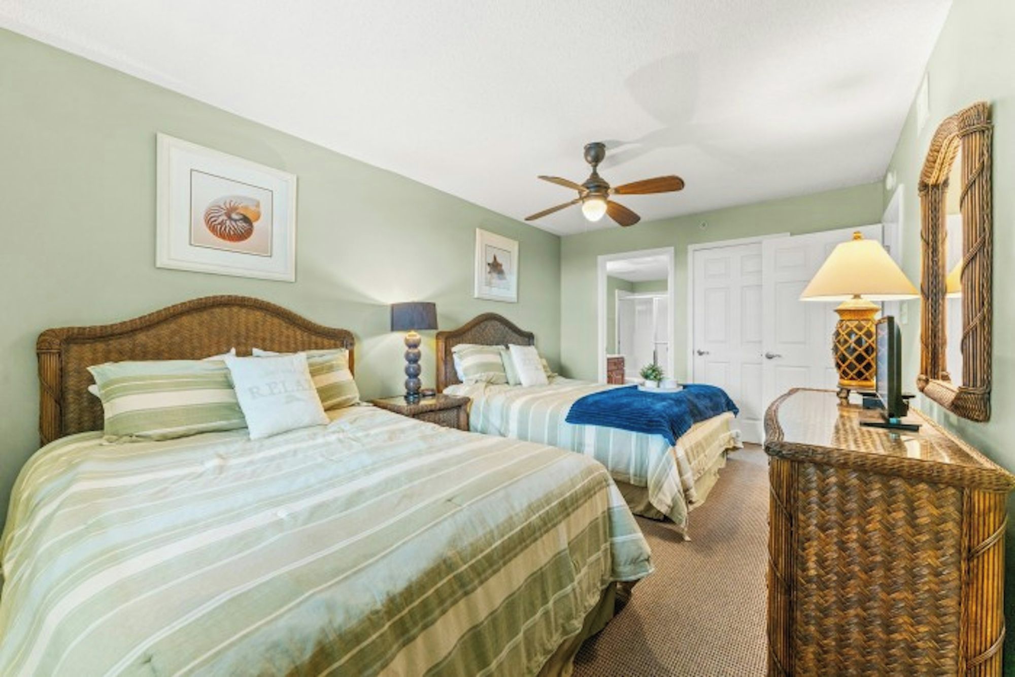 A hotel room with two beds, a ceiling fan, a lamp, and a mirror.