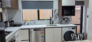 Eine kompakte Küche mit integriertem Geschirrspüler, einer Mikrowelle und einem Fenster mit Holzjalousien.